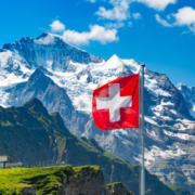 Schweizer Flagge vor blauem Himmel und Bergen
