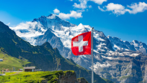 Schweizer Flagge vor blauem Himmel und Bergen