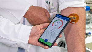 Patch mit Sensor auf einem Männerarm, mit dem Smartphone werden die Daten ausgelesen